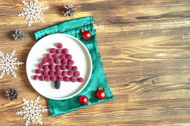 Funny Christmas tree shaped sweet fresh raspberry berry on plate on wooden background for kids children breakfast. xmas food with new year decorations copy space