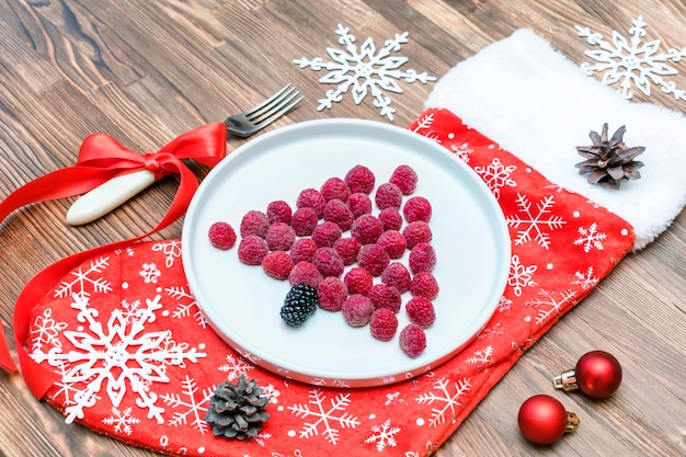 Funny Christmas tree shaped sweet fresh raspberry berry on plate on wooden background for kids children breakfast. xmas food with new year decorations