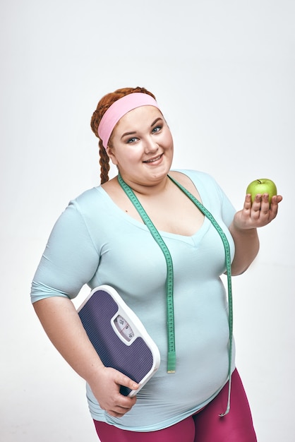 Funny chubby woman is holding an apple and scales