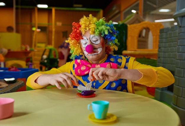 Фото Забавный клоун играет с игрушечным чайным набором в детской игровой комнате
