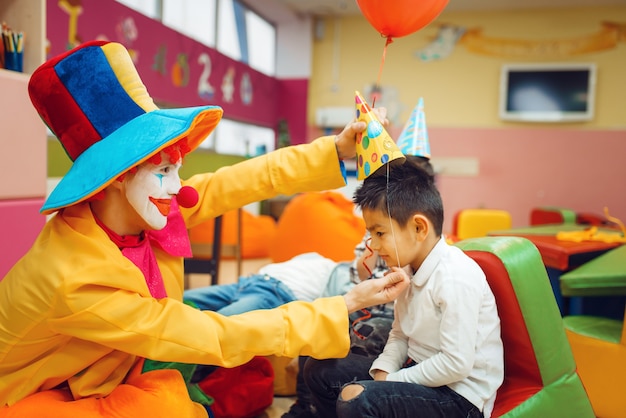 Funny clown puts a cap on the little boy's head.