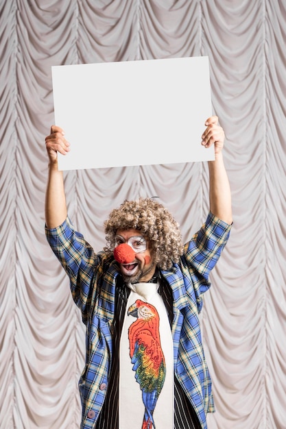 Foto un clown divertente mostra un cartello bianco vuoto per l'iscrizione un clown in piedi sul palco
