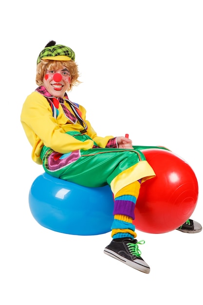 Photo funny clown sits on blue and red rubber balls isolated on the white background