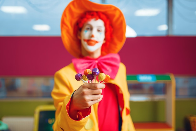 Photo funny clown with lollipops in hand poses in children's area.