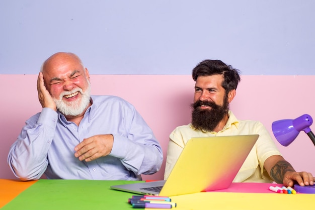 Funny colleagues having fun sitting at desk with laptops Excited business man in office with colleagues Funny office workers Old man getting good news