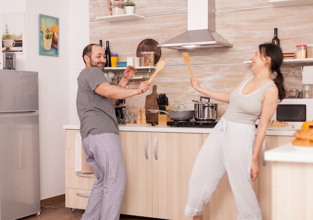 Coppie divertenti che ballano in cucina durante la colazione indossando il pigiama. moglie e marito spensierati che ridono divertendosi divertendosi godendosi la vita autentiche persone sposate positiva relazione felice