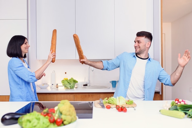 Funny couple fight with baguettes while cooking at home together husband and wife feeling playful at kitchen