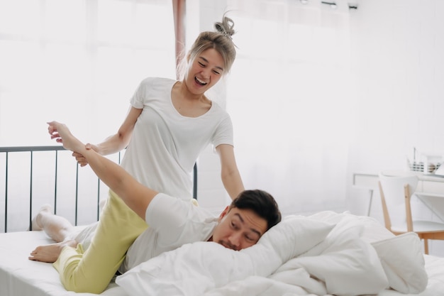 Funny couple wife giving husband hurt massage in white bedroom