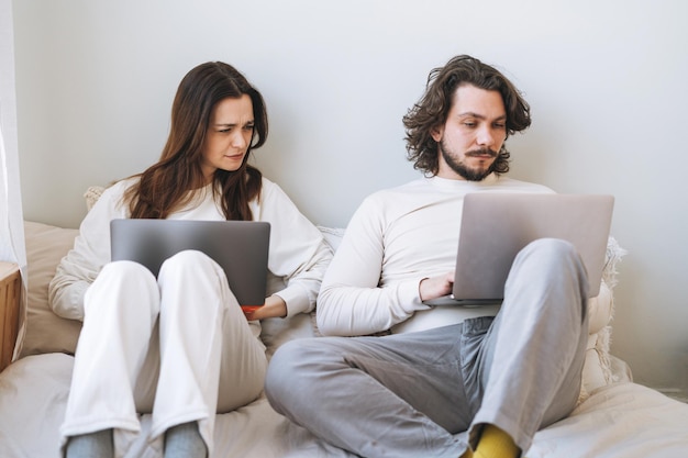 Funny couple young family using laptops on bed in bedroom at the home