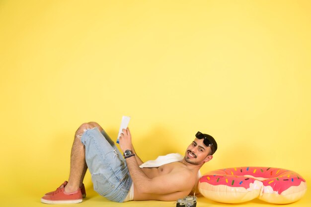 Funny crazy man with inflatable circle pretends to float on light yellow background.