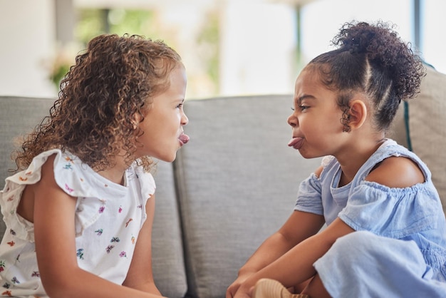 面白いクレイジーで愚かな子供たちは、家のリビングルームのソファで一緒に遊んで楽しんでいます.ラテン系の子供や姉妹は舌を突き出し、居心地の良いソファと快適な家族の家で子供時代を楽しんでいます.