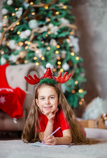 Una ragazza caucasica carina e divertente, mancina, scrive una lettera a babbo natale vicino all'albero di natale