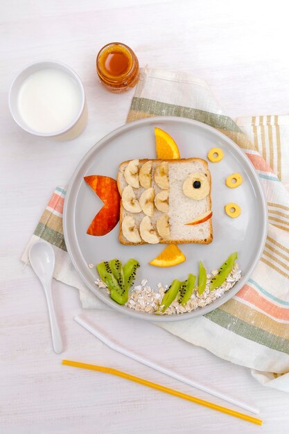 Pane tostato a forma di pesce carino divertente con banana, mela, latte, arancia, miele, bambini, bambini, dolce, dessert, colazione sana, pranzo, cibo, arte, su sfondo platewooden, vista dall'alto ravvicinata