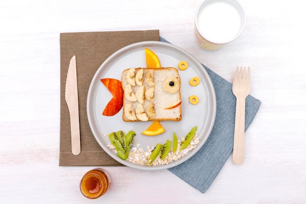 Забавная милая рыбная форма сэндвич тост хлеб с бананом яблоком оранжевым молоком мед для детей сладкий десерт для младенцев здоровый завтрак обед еда искусство на тарелке деревянный фон близкий взгляд вверх