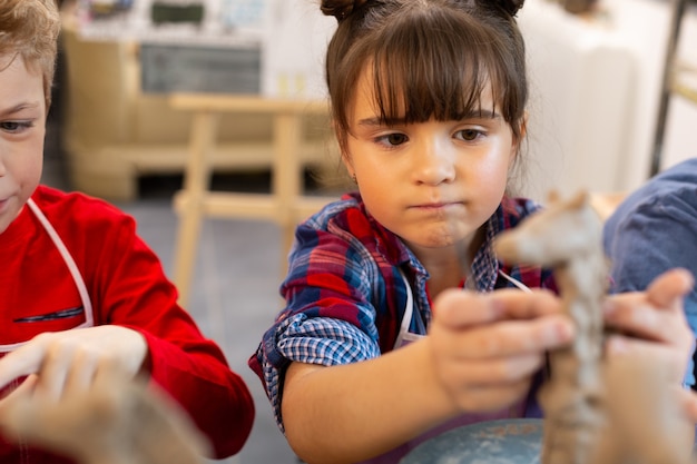 Funny cute girl modeling clay animals at art lesson