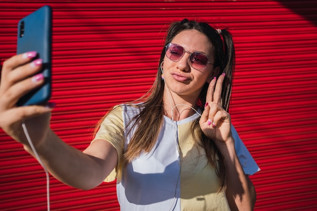 Una ragazza divertente e carina si fa un selfie e mostra due dita che fanno il segno di pace.