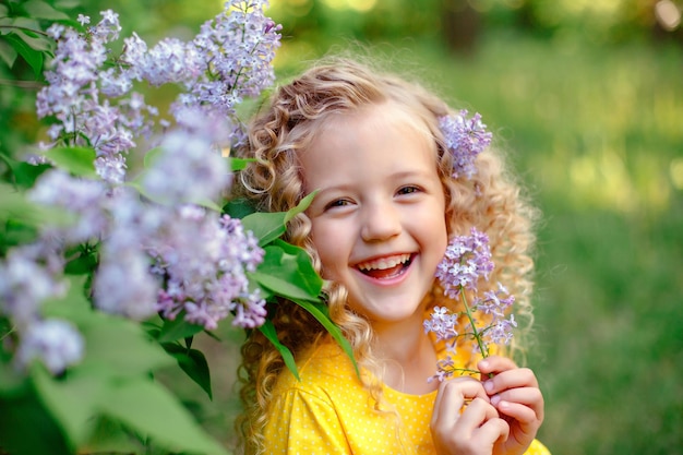 Funny cute laughing little girl in spring in a blooming lilac garden