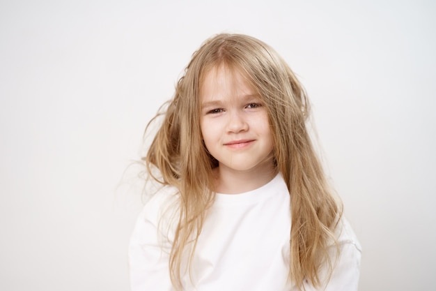 Funny and cute little girlwith shaggy long hair on a white background. shampoo and balm for children. cosmetics for girls. light brushing.