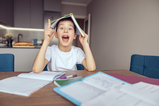 Funny cute smart caucasian boy holding textbook above head having idea know solution