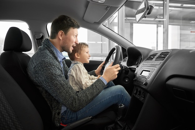 Funny daddy and son sitting on seat of drivers in new auto