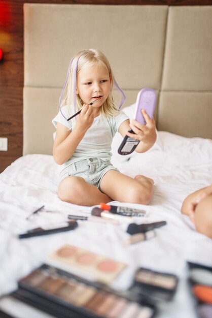 Funny daughter playing with mothers makeup in bed at home. A truly carefree childhood, happy time