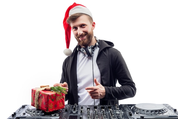 Funny dj guy in santas hat holds gift box while standing behind a turntable new year party