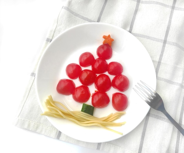 Funny edible Christmas tree made of tomatoes and spaghetti breakfast idea for kids.