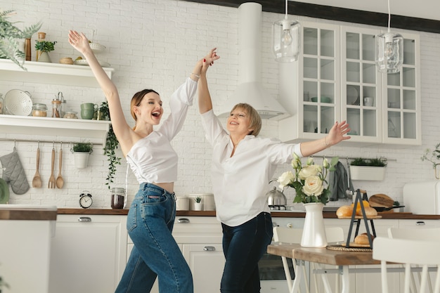 Funny elderly mother is having fun in the kitchen with an adult daughter