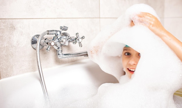 Funny emotional caucasian little girl washes her head with lots