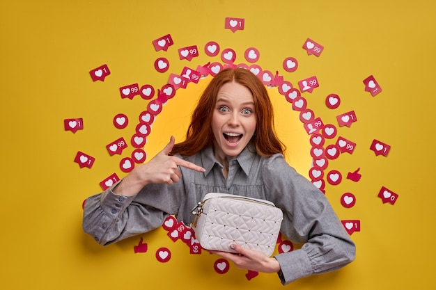 Funny excited female pointing at a purse, isolated on yellow wall, get a lot of likes