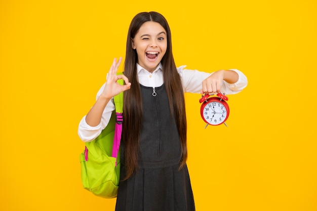 Funny face Back to school Teenager school girl with backpack hold clock alarm time to learn School children on isolated yellow background