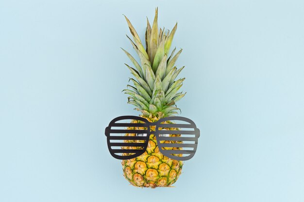 Foto faccia buffa di ananas con gli occhiali sul blu