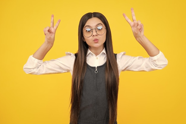 Funny face Teenager child girl showing fingers victory sign Number two vsign symbol isolated on yellow background