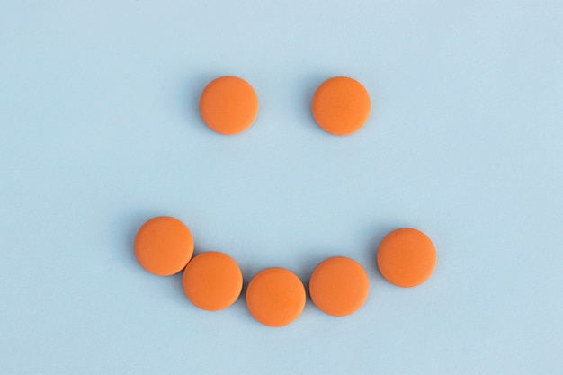 Funny faces of orange pills on a blue background. Concept of antidepressants