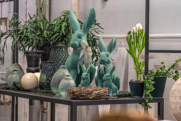 A funny family of bunnies in mint color glass and porcelain eggs a basket of birch branches a white tulip in a pot green plants in a vase on a shelf