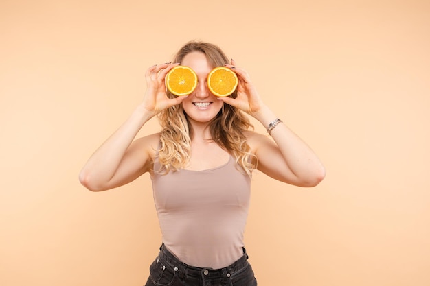 Ragazza alla moda divertente con le arance della tenuta dell'acconciatura sugli occhi.