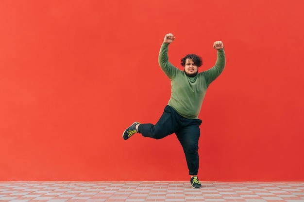 Funny fat guy dancing on a red wall and listening to music on headphones