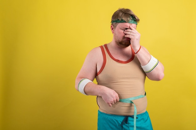 funny fat man in sportswear takes measurements of body volume.