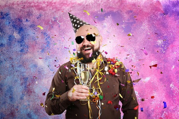 Funny fat man with party hat and glass of champagne on color background