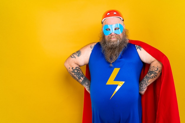 Funny fat man with superhero costume acting as superhuman with special powers portrait on colored wall