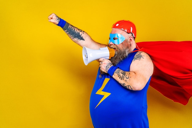 Funny fat man with superhero costume acting as superhuman with special powers portrait on colored wall