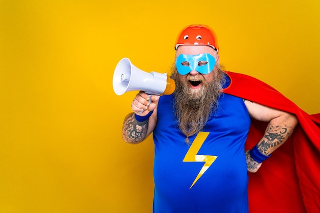 Funny fat man with superhero costume acting as superhuman with special powers portrait on colored wall