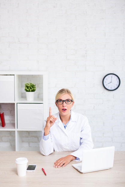 Funny female doctor or scientist showing idea sign in office copy space over white wall