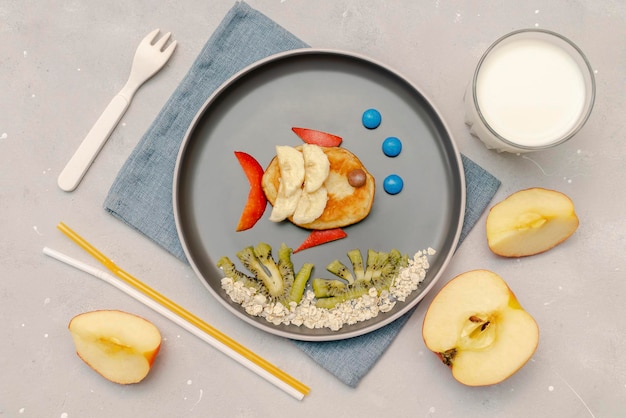 Spuntino a forma di viso di pesce divertente da pancakebananaapples sul piatto bambini carini bambini per bambini dolce colazione dessert pranzo sano cibo arte con milkkiwi su sfondo grigio cemento vista dall'alto