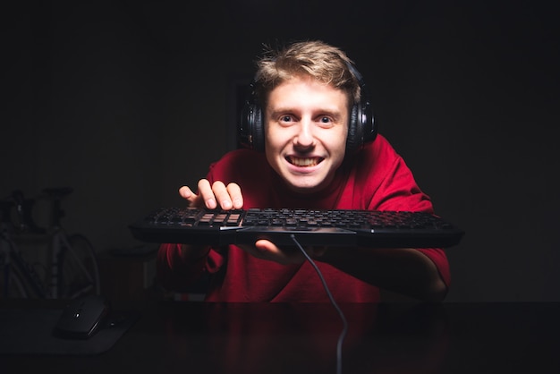 Funny gamer sitting at home at night and playing video games with a keyboard in his hands