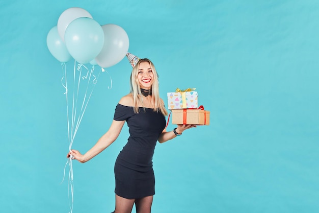 Funny girl in birthday hat on blue background Portrait of attractive cute cheerful girl wearing party cone with balls