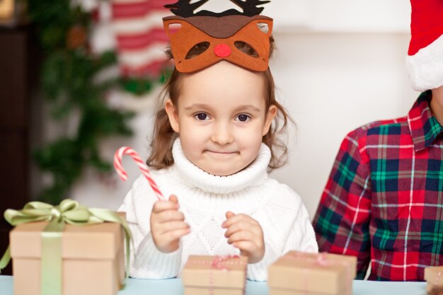 Photo funny girl in a christmas deer mask holding candy cane in a hand.