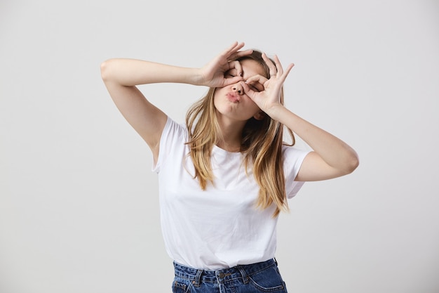 Funny girl dressed in a white t-shirt and jeans makes glasses with her hands on her eyes