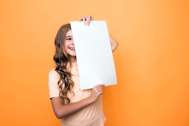 Забавная девушка держит чистый лист бумаги на оранжевом фоне, макет для надписи