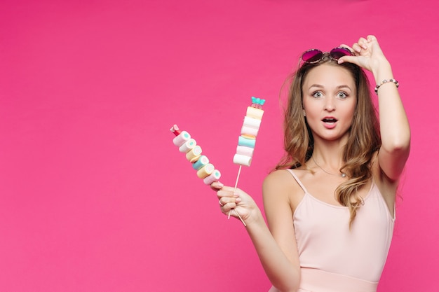 Funny girl holding marshmallows on stick under head, having fun.